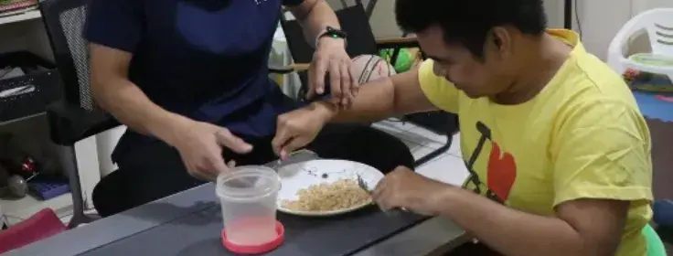 Therapist guiding a young man in practicing independent eating skills with a fork and spoon