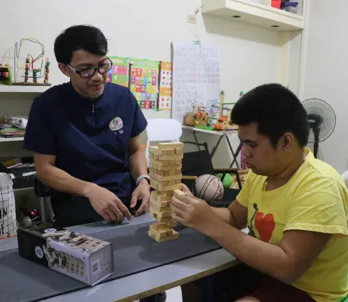 Therapist guiding a young man through a focused block-stacking activity in the therapy room
