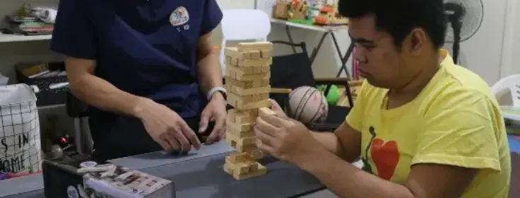Therapist guiding a young man through a focused block-stacking activity in the therapy room