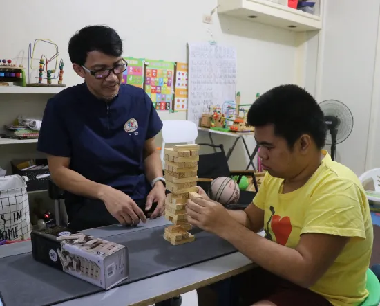 Therapist guiding a young man through a focused block-stacking activity in the therapy room